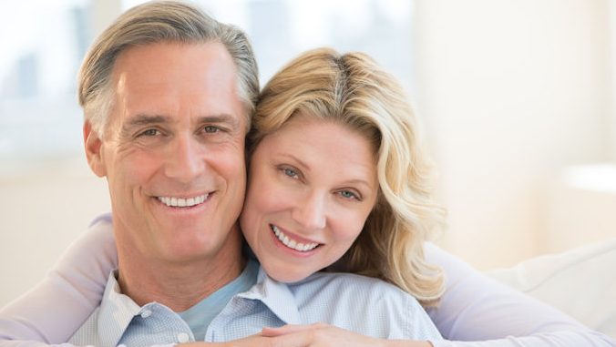 Portrait of loving mature woman embracing man from behind at home